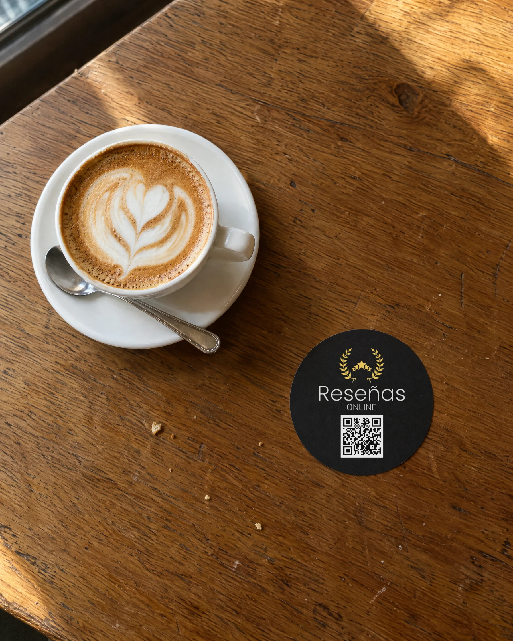 Pegatina negra con el logo de Reseñas Online y un código QR sobre la mesa de una cafetería junto a un café